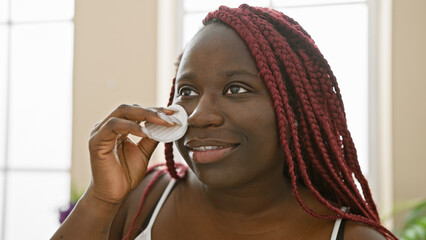 Wall Mural - African american woman with braids applying makeup indoors, showing beauty, femininity, and daily routine.