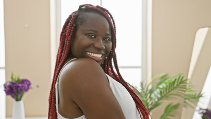 Poster - Smiling african woman with braids in a bright indoor living room setting.