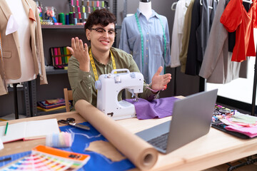 Poster - Young non binary man dressmaker designer on video call with laptop celebrating achievement with happy smile and winner expression with raised hand