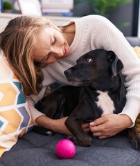 Wall Mural - Young blonde woman hugging dog sitting on sofa at home