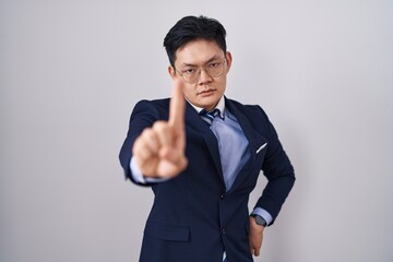 Sticker - Young asian man wearing business suit and tie pointing with finger up and angry expression, showing no gesture