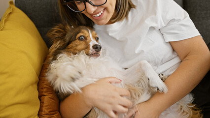 Canvas Print - Hispanic woman cuddling with dog in a cozy living room setting, depicting friendship and comfort.