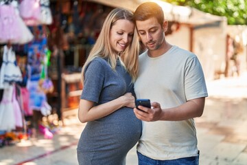 Canvas Print - Man and woman couple expecting baby using smartphone at street market
