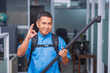 © Mdv Edwards - Confident janitor in blue uniform gives an okay sign while holding the nozzle of a backpack vacuum cleaner in an office.