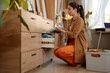 © Seventyfour - Full length side view portrait of young woman putting away clean clothes in drawer on laundry day, copy space
