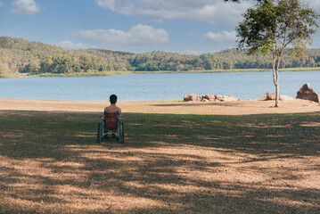 Wall Mural - Back of young boy sitting on wheelchair looking at beautiful nature park, Traveling using a wheel chair to learn about the world without limits with support from family,Good mental health,positive pic