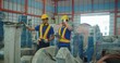 Industrial workers with tablet and headset in warehouse, evaluate machinery wrapped in protective plastic in an industrial warehouse during a quality check.