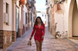 © Manuel - Young, beautiful and dark-haired woman in an elegant red dress and heels in her hand, walking barefoot, at dawn along a lonely street of a beautiful white Andalusian village. Concept beauty, fashion.
