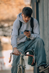 Poster - young urban outfit riding a bicycle with mobile phone