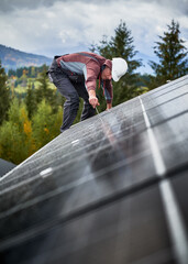 Wall Mural - Man mounter mounting photovoltaic solar panels on roof of house. Engineer in helmet installing solar module system with help of hex key. Concept of alternative, renewable energy.