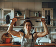 Hard homework of tired housewife - strong woman lifting weight barbell in kitchen with copy space