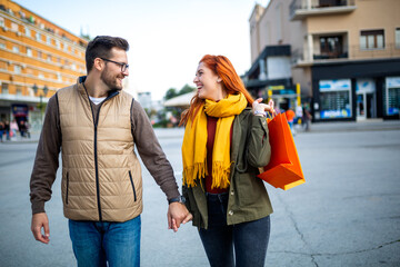 Wall Mural - Smiling couple enjoying having fun walking and exploring city street during the day with shopping bags