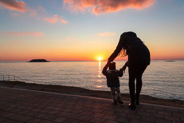 Wall Mural - Silhouette of loving mother with small toddler walking on idyllic beach at sunset in coastal town Funtana, Istria, Croatia. Calm water surface of Adriatic Mediterranean Sea. Family vacation concept