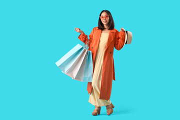 Poster - Happy beautiful young Asian woman with shopping bags on blue background