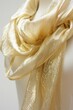 Delicate, shimmering gold scarf elegantly draped around the neck of mannequin on a white background. The fabric has a subtle sheen and texture that adds to its allure.