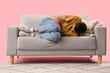 © Pixel-Shot - Young man suffering from bellyache on sofa against pink background