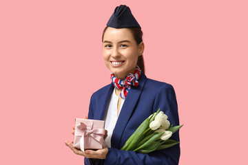 Canvas Print - Young stewardess with white tulips and gift box on pink background. Women's Day celebration