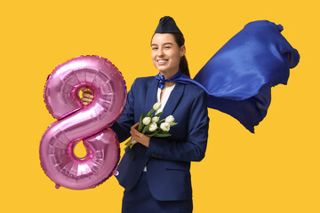 Poster - Young stewardess with superhero cloak holding balloon in shape of figure 8 and white tulips on yellow background. Women's Day celebration