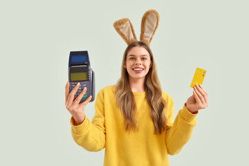 Sticker - Young woman in bunny ears with payment terminal and credit card on light background. Easter Sale