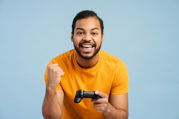 Joyful African American man holding joystick, making victory gesture with fist and looking at camera