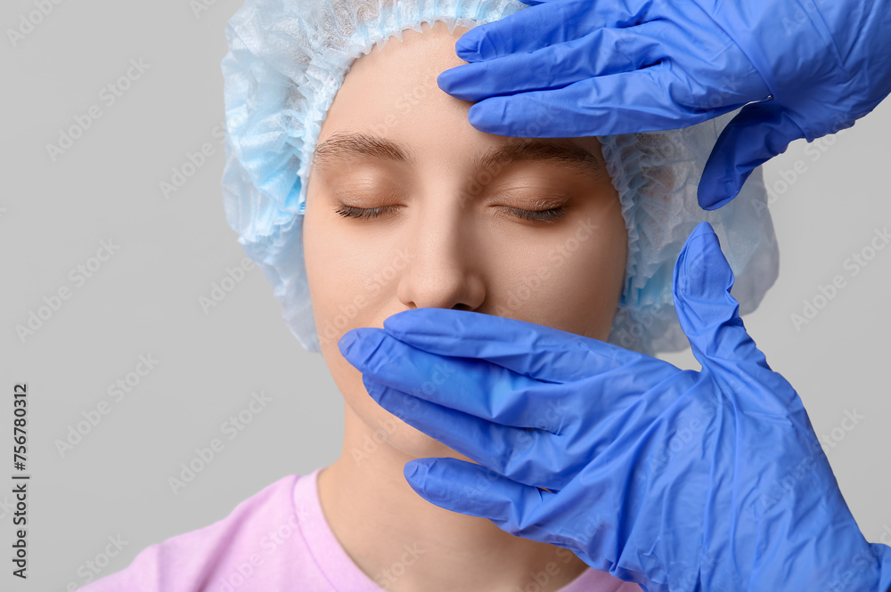 Plastic surgeon examining woman's face on grey background, closeup. Blepharoplasty concept