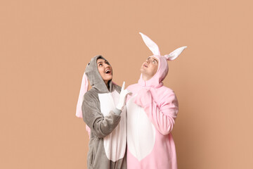 Wall Mural - Beautiful young couple in bunny costume pointing at something on brown background. Easter celebration