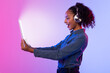 © Prostock-studio - Joyful lady with headphones using tablet, lit screen, gradient background