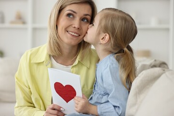 Wall Mural - Little daughter kissing and congratulating her mom with greeting card at home. Happy Mother's Day