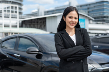 Wall Mural - Young beautiful asian business woman buying new car. she was standing in near car on the roadside downtown city background. Smiling business female driving vehicle on the road on a bright day