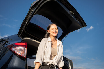 Wall Mural - Young beautiful asian women buying new car. she was sitting at trunk of car. Beautiful moment blue sky Smiling female driving travel by vehicle on the road on a bright day weekend with sun light.
