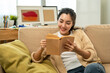 © Chanakon - Asian beautiful woman sitting reading book on cozey couch sofa in living room with sun light morning. People female stay home part time relax at home.