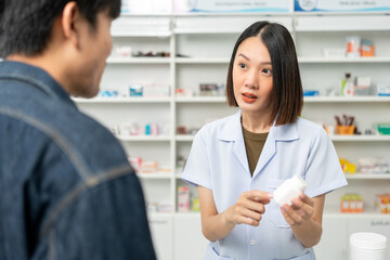 Pharmacist recommends medicines to customers.Taking the questions of medication. Asian female pharmacist giving prescription medications to customers at drugstore shelves.