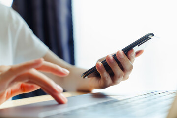 Wall Mural - Woman using smartphone and hand typing on the computer keyboard in the office.