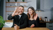 Happy young couple sit in the kitchen make video call looking at camera wave hands greeting, talking with friends modern tech users chatting with remote distant relatives. Webcam view	