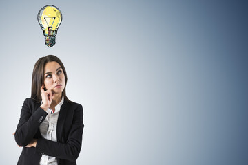 Poster - Attractive thoughtful young female with creative lamp sketch on gray wall background with mock up place. Idea, creativity and innovation concept.