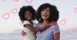Image of happy african american mother and daughter embracing at beach over hearts