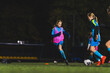© PoppyPix - young girls in blue uniforms playing soccer on a grassy field at night, teamwork in sport. High quality photo