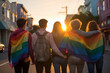 Back view of a close-knit group of friends draped in a pride flag, walking together as the day ends in a beautiful urban sunset, celebrating pride month. 

