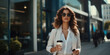 A stylish woman in a white business suit walks down the street holding a disposable cup of coffee in her hand.