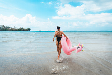 Wall Mural - Summer travel, woman holding an inner tube, walking in the middle of the sea