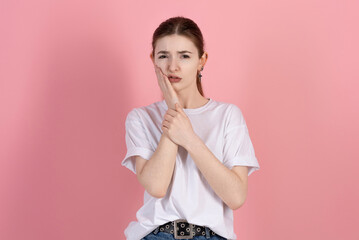 Wall Mural - Attractive Caucasian young brunette woman in casual white t-shirt touching cheek and suffering due to toothache isolated on pink studio background. Medicine, dentistry.