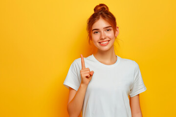 Sticker - Portrait of a young girl points her finger up on a yellow background. Copy space