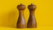 Two wooden salt and pepper mills resting on a vibrant yellow background