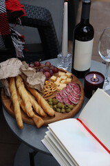 rest and relaxation. red wine, glasses, book, candles and snacks are on the table. romantic dinner on the terrace. aesthetic photo. wooden board with grapes, cheese, sausage, olives and grisini