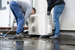 © Connect Images - Two technicians installing an outdoor unit of a heat pump on a rooftop.