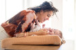 © Connect Images - A woman is smiling and interacting with a baby lying in a basket-type crib in a brightly lit room.