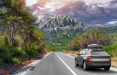 Wall Mural - Travel car drives along the highway against the backdrop of rocky mountains on a sunny day.