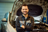 Fototapeta Miasto - Portrait of a mechanic man smiling for the camera, standing in front of the opened hood.