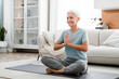 © InsideCreativeHouse - Middle-aged woman meditating in lotus position while having training at home on fitness mat. Female athlete praying breathing while doing yoga indoors