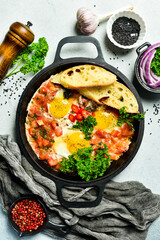 Wall Mural - Fried eggs. Shakshuka middle east meal in iron frying pan with toasted bread, pepper, chili, tomato and garlic. Gray concrete table. Top view. Close up